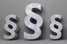 Drei große steinerne Absatzsymbole sind vor einer grauen Wand angeordnet, wobei das mittlere Symbol das größte ist.